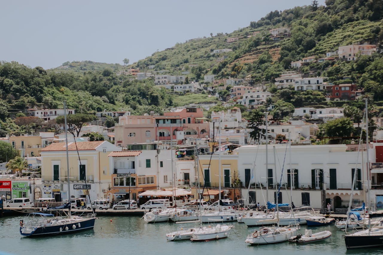 Scenic marina with sailboats and traditional hillside houses under clear blue skies.